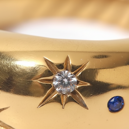 Gold ring with star designs and embedded gemstones on a blurred background